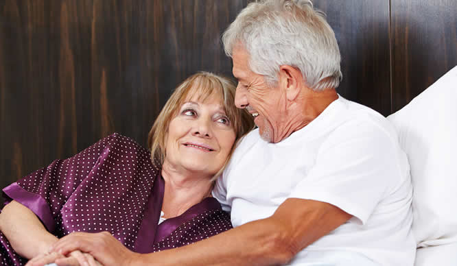 Ein älteres Ehepaar blickt sich im Bett verliebt an