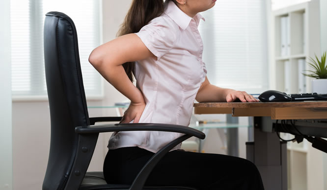 Eine Frau am Schreibtische hat Rückenschmerzen
