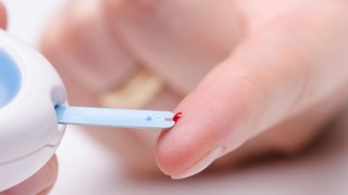 Der Blutzuckerspiegel wird über einem Blutstropfen am Finger gemessen