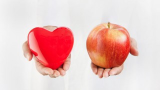 Eine Ärztin hält einen Apfel und ein Herz aus Plastik